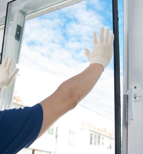master in protective gloves, changing a double-glazed window in a plastic window, side view, against the blue sky